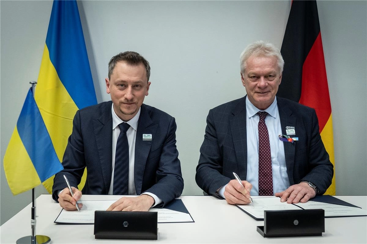Два чоловіки підписують документи на тлі прапорів України та Німеччини під час міжнародної виставки